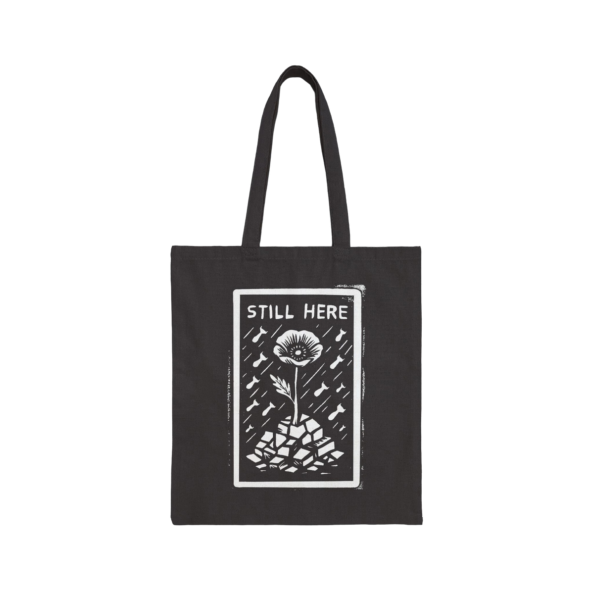 The Still Here Tote Bag displays a white hand-drawn flower rising from stones amid falling rain, symbolizing resilience again
