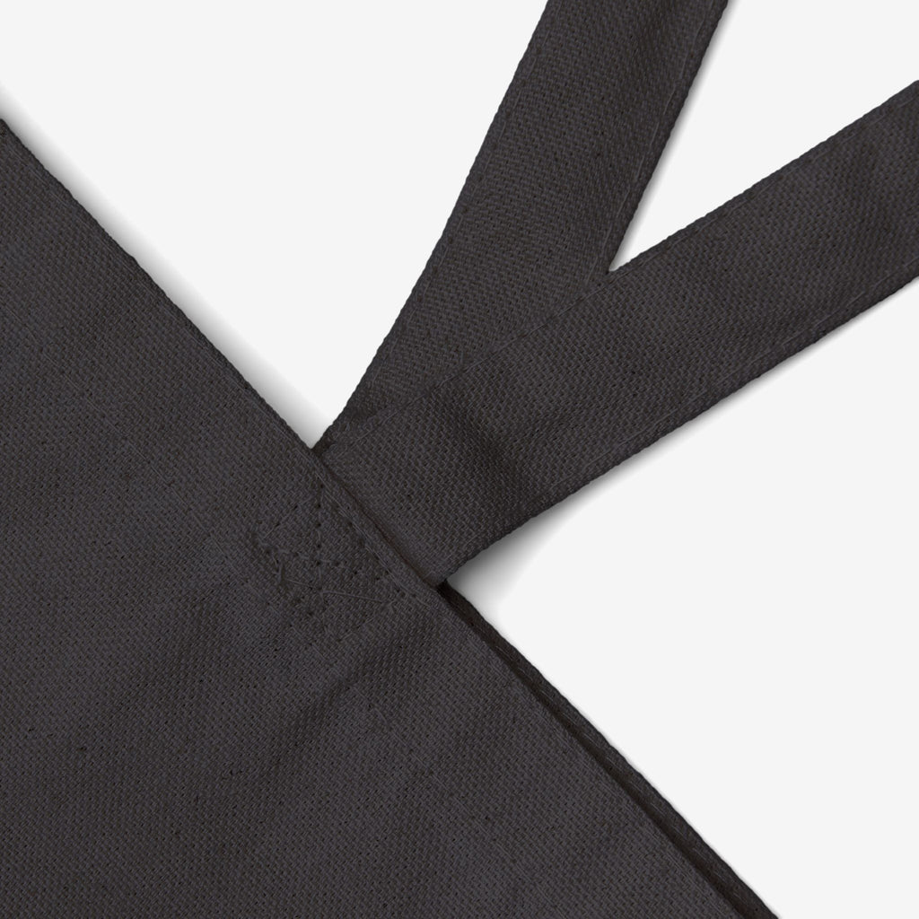 Still Here Tote Bag showcasing reinforced stitching on a black cotton canvas upper corner, with a meaningful design of a flower amid rubble, symbolizing resilience against violence.
