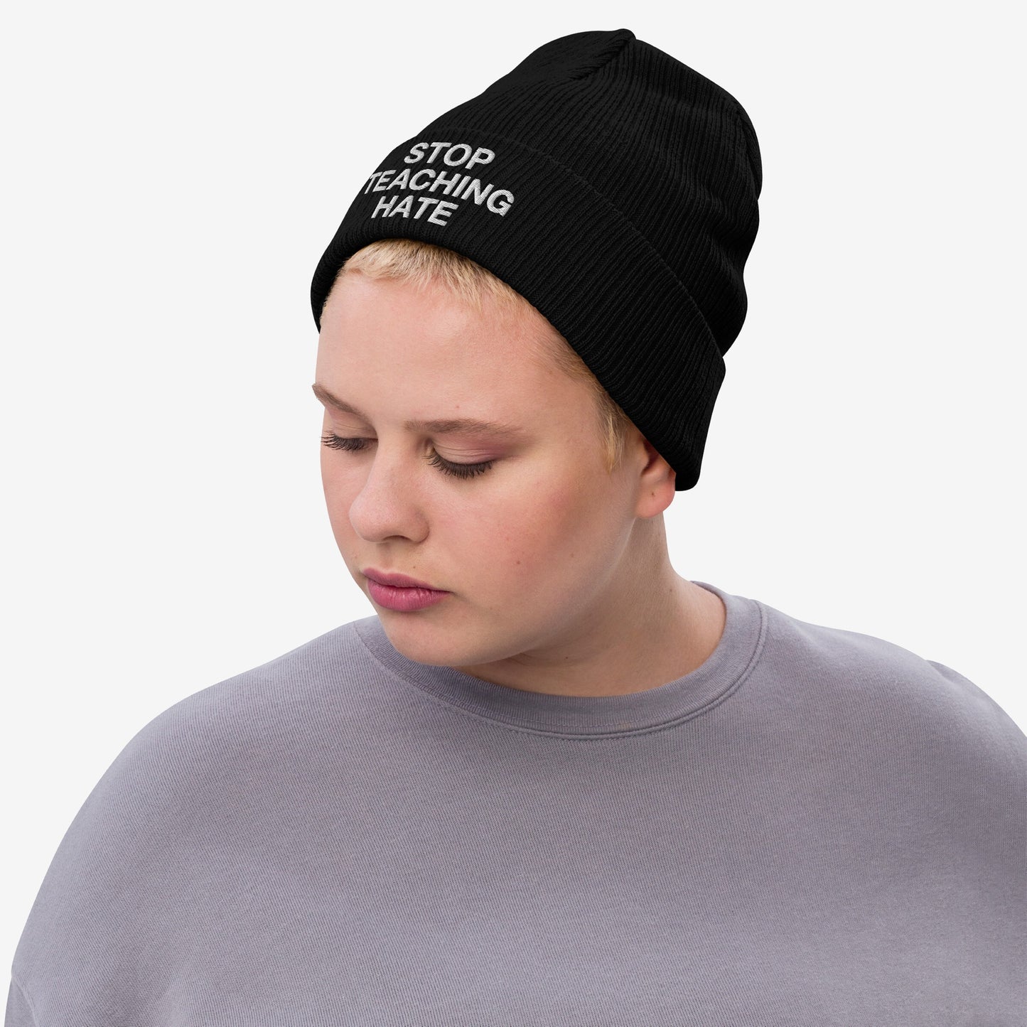 Person wearing the Stop Teaching Hate Hat, a black knit beanie with the message “STOP TEACHING HATE” embroidered, embodying a statement against hate, reflecting commitment to equality and resistance.