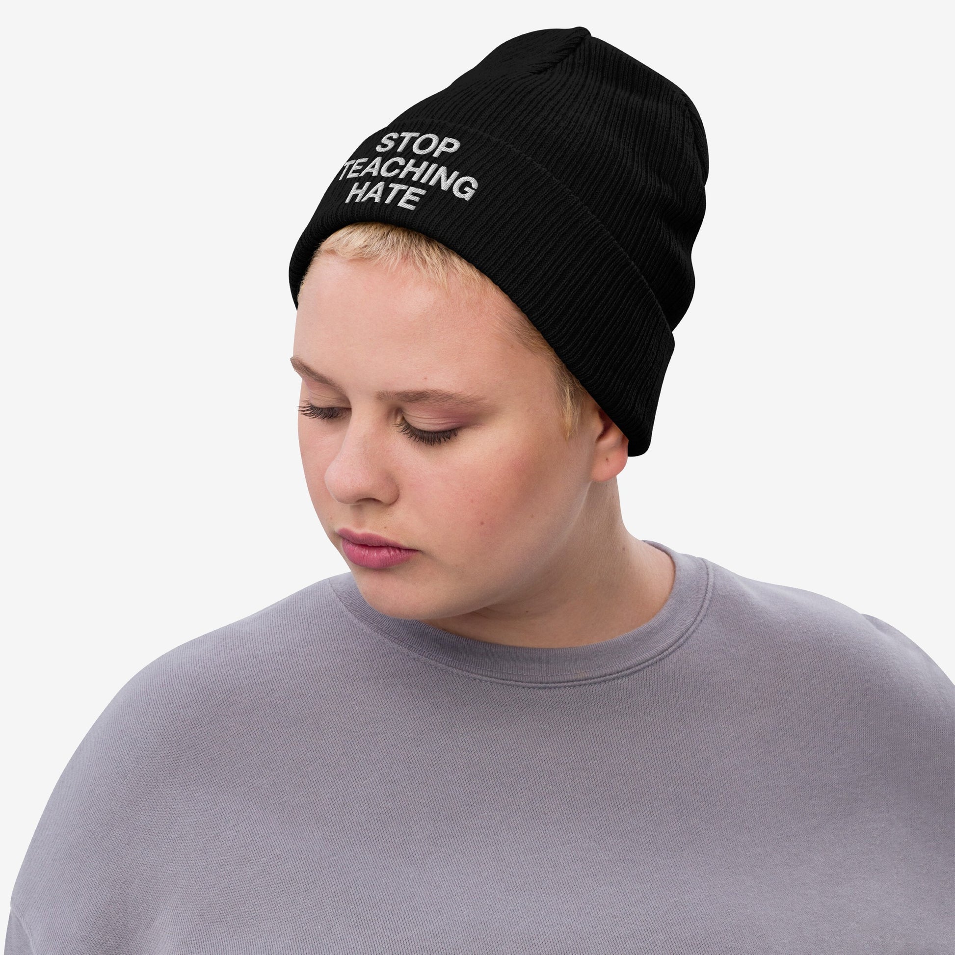 Person wearing the Stop Teaching Hate Hat, a black knit beanie with the message “STOP TEACHING HATE” embroidered, embodying a statement against hate, reflecting commitment to equality and resistance.