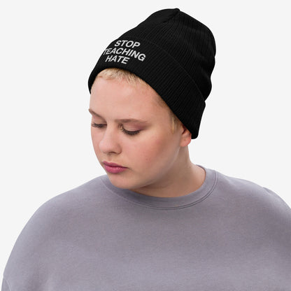 Person wearing the Stop Teaching Hate Hat, a black knit beanie with the message “STOP TEACHING HATE” embroidered, embodying a statement against hate, reflecting commitment to equality and resistance.