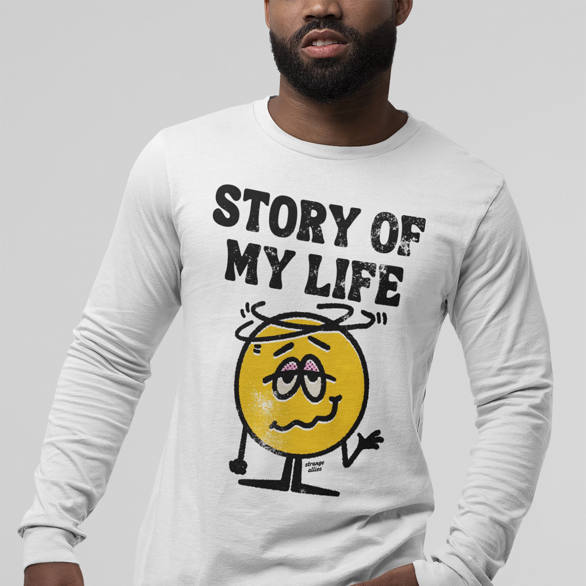 Story Of My Life Shirt featuring a distressed yellow smiley with swirls, shrugging. Bold text above reads 'STORY OF MY LIFE'. Signed 'strange allies', this tee humorously captures life’s chaotic moments.