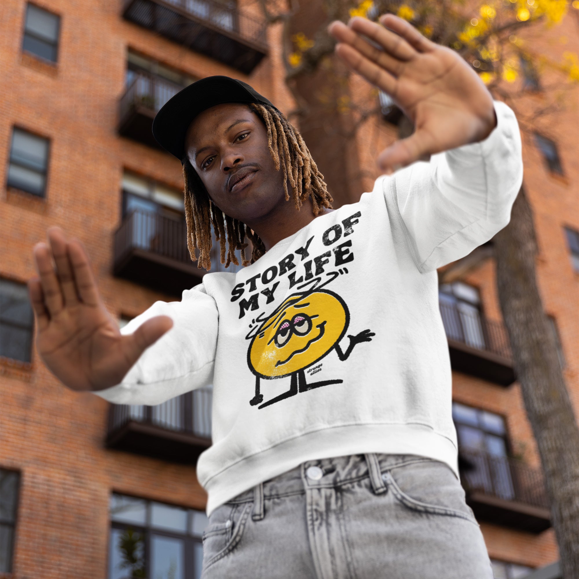 Young man models the Story Of My Life sweatshirt featuring a cartoonish yellow face with a relatable slogan, embodying humor and resilience. Perfect for expressing life's chaos with a sarcastic twist.