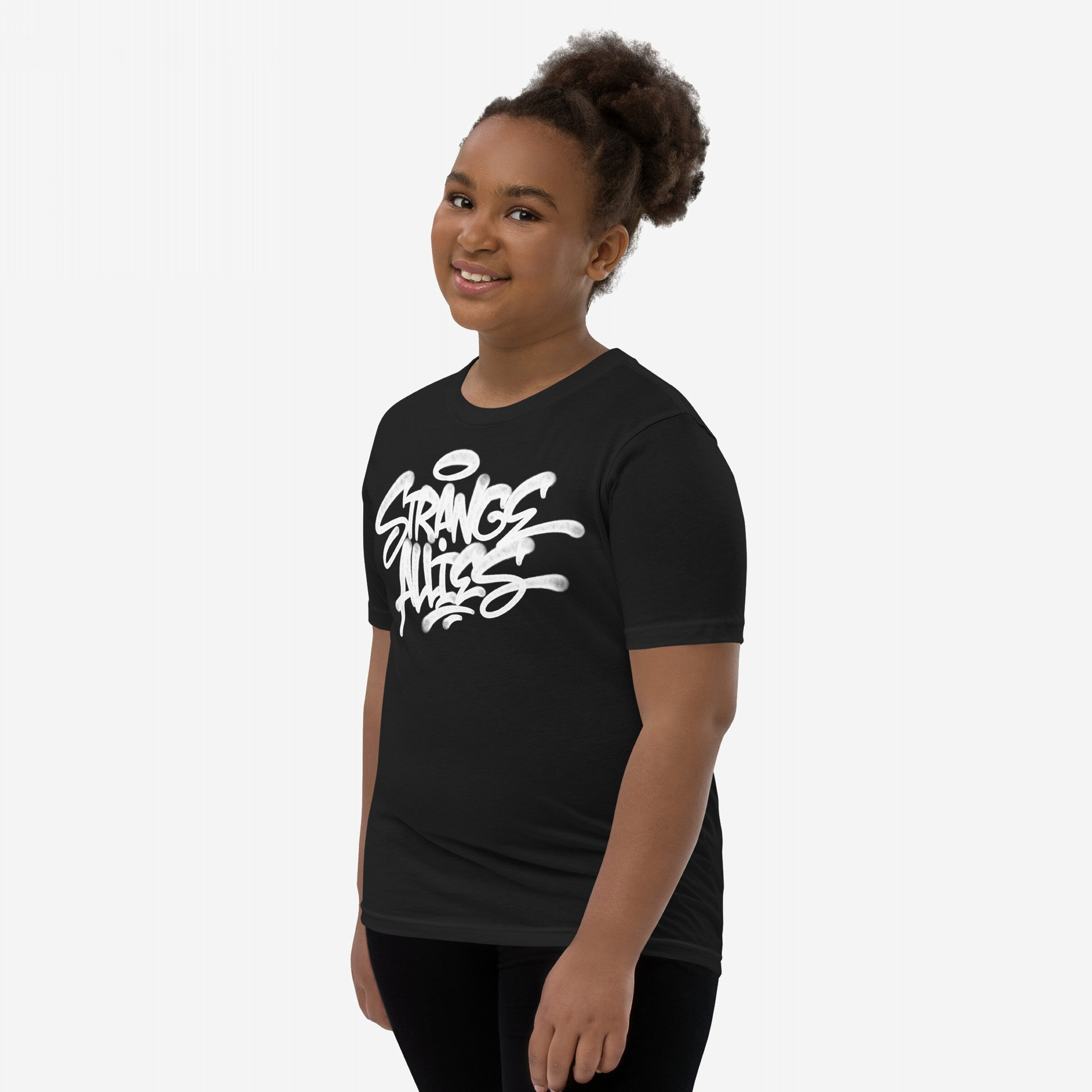 Young girl wearing the Strange Allies Handstyle T-shirt, featuring a white graffiti-style logo Strange Aliens on black. She smiles confidently, embodying the shirt's rebellious, inclusive spirit.