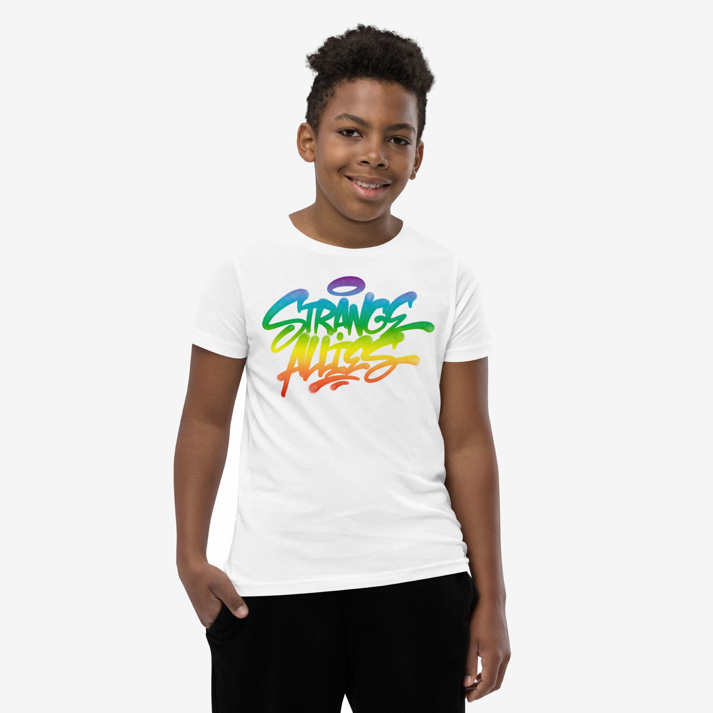 Young boy in the Strange Allies Rainbow Handstyle T-shirt, featuring a graffiti-style STRANGE ALIENS design with a rainbow gradient and halo graphic. He's casually posed with a hand in his pocket.