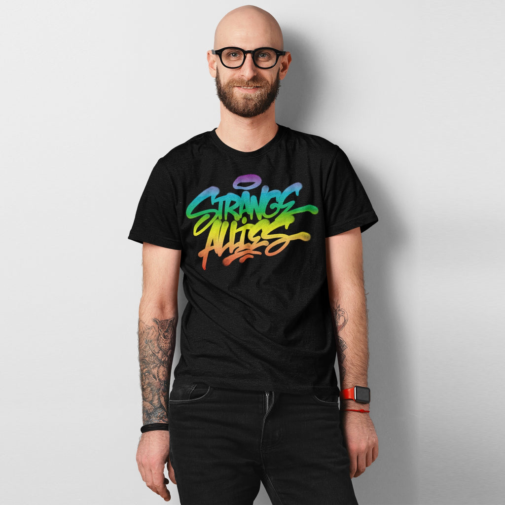 Smiling man wearing a Strange Allies Rainbow Handstyle T-shirt with vibrant graffiti script, showcasing tattoos and a red smartwatch, embodying bold individuality and inclusivity.