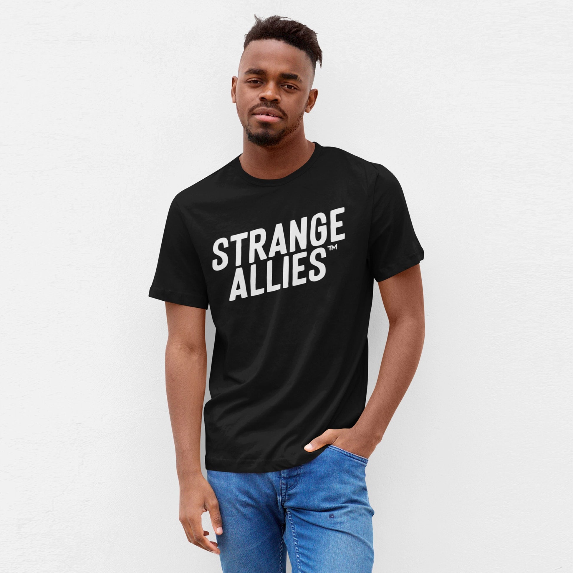 Young man in a black Strange Allies T-shirt with bold white lettering, paired with blue jeans, embodying a statement of individuality and support for diverse communities.