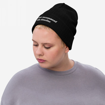 A person wears the Timeline Hat, a black ribbed knit beanie with do not recommend this timeline embroidered on the brim, embodying a statement of political discontent and sarcasm.