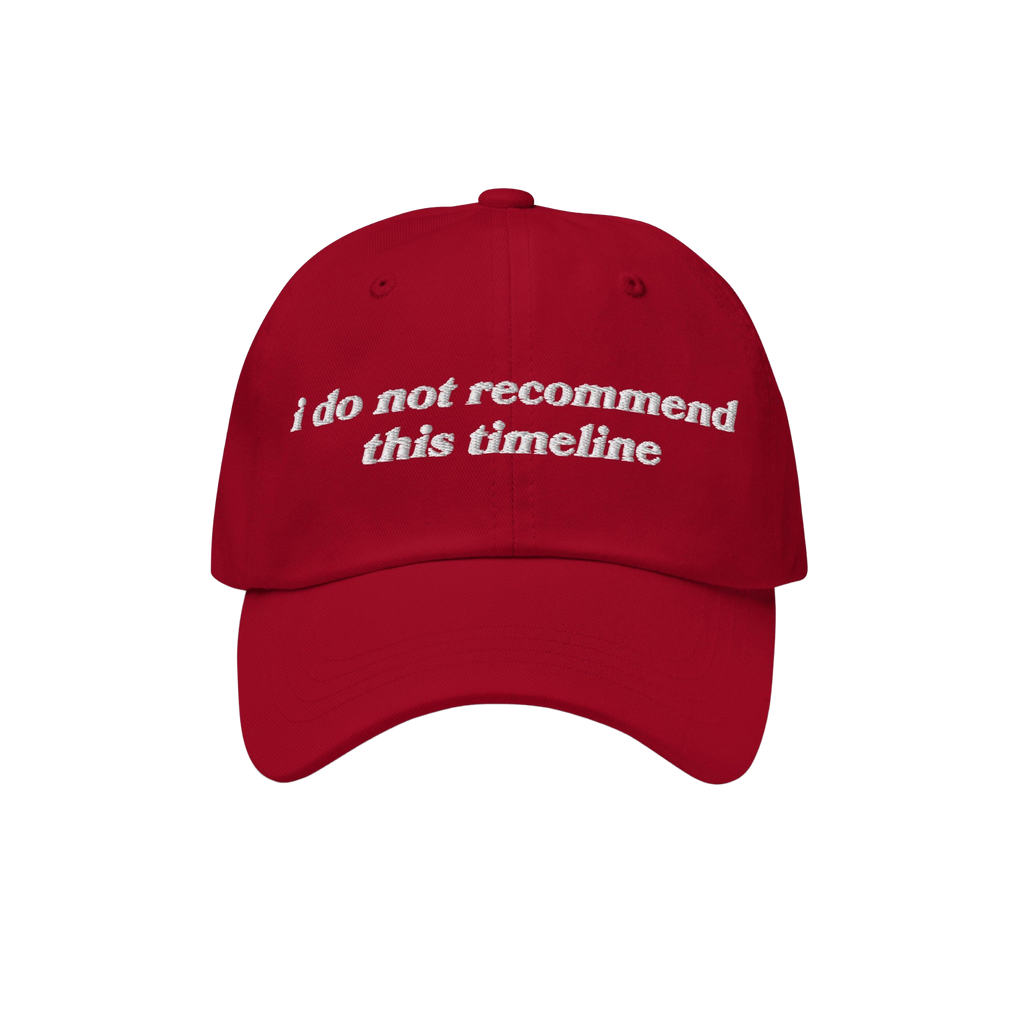 Red six-panel baseball cap with white embroidery reading “i do not recommend this timeline”. Ideal for political humor en