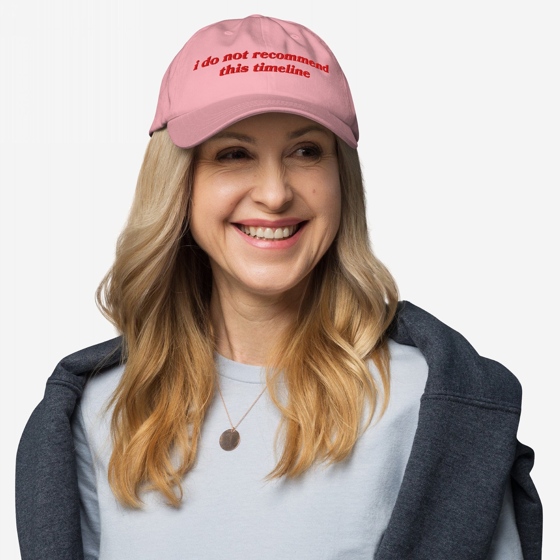 Smiling woman wearing the Timeline Hat with the phrase “i do not recommend this timeline” embroidered, reflecting a sarcastic stance against current events. Ideal for expressing political dissatisfaction.