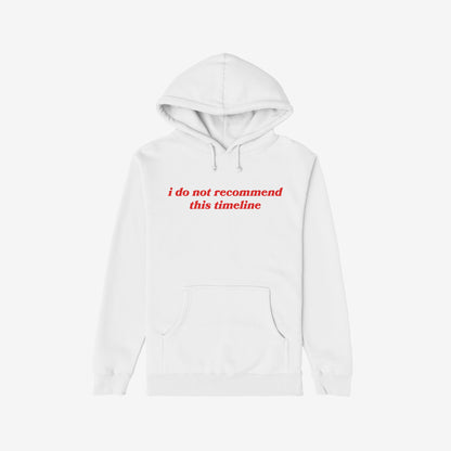 Plain white Timeline Shirt hoodie with red serif text stating “i do not recommend this timeline,” capturing humor and critique, reflecting disillusionment and vintage flair. Features kangaroo pocket and drawstring hood.