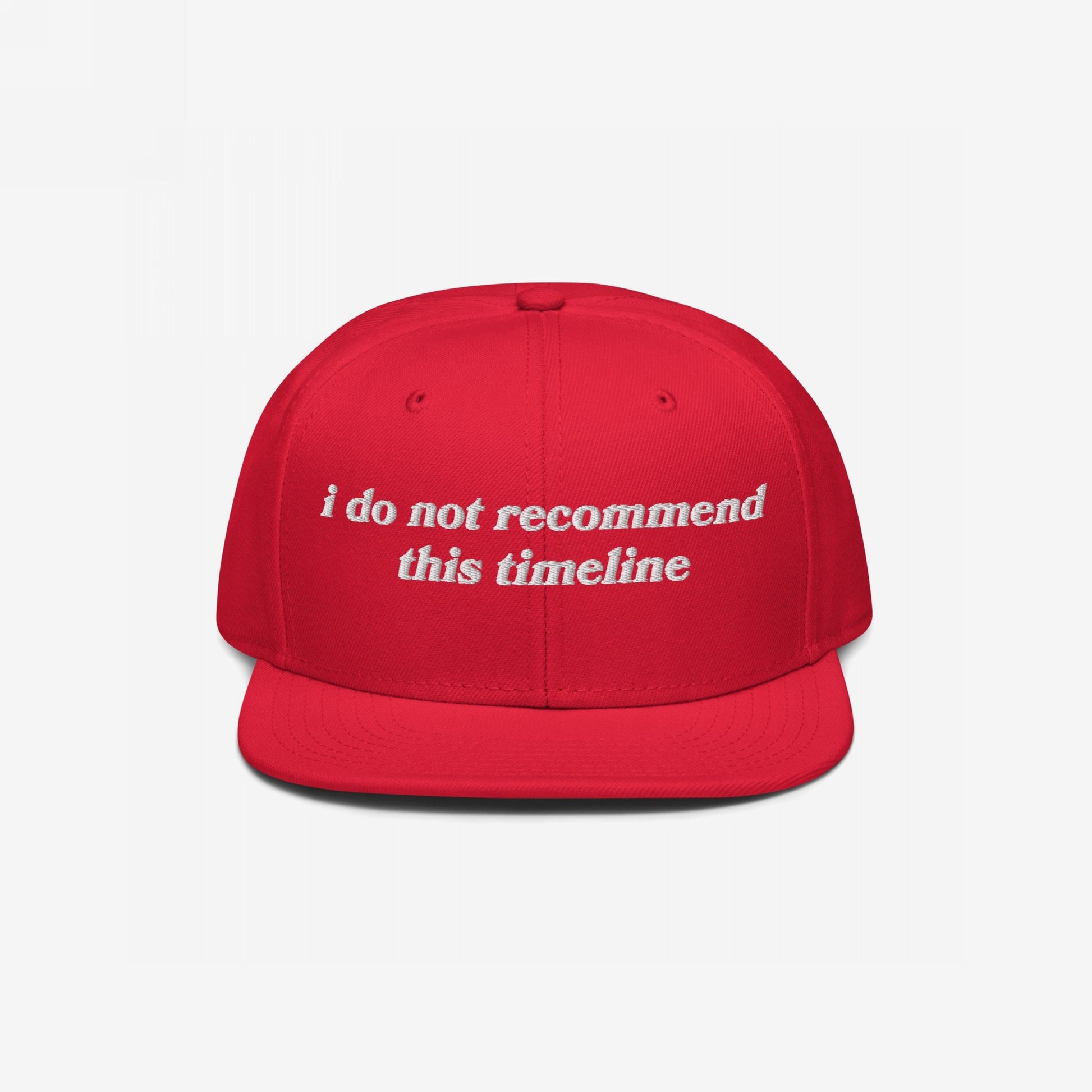 Red flat-bill snapback cap with white embroidered text: “I Do Not Recommend This Timeline.” This Timeline Hat conveys political sarcasm, perfect for expressing discontent with style.