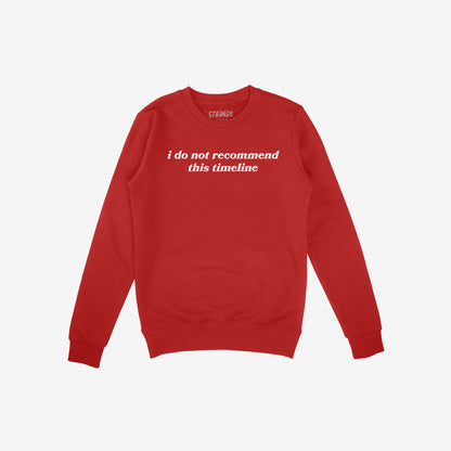 Red long-sleeve crewneck sweatshirt with white text “I do not recommend this timeline.” The Timeline Shirt humorously critiques modern life, capturing skepticism with style. Proceeds support NAMI, advocating mental health awareness.
