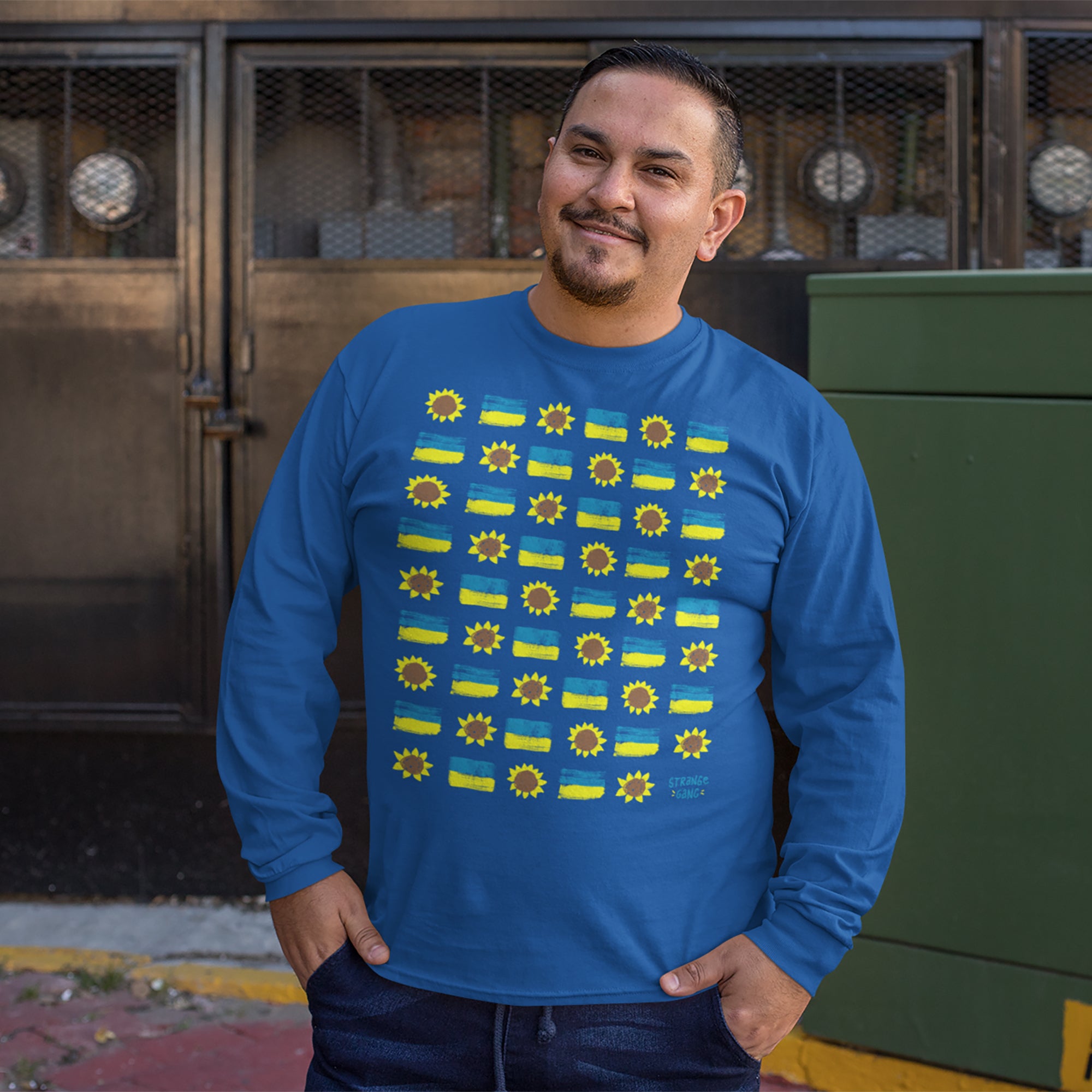 A man wearing the Ukraine Sunflowers Shirt, featuring a grid of sun shapes and stripes symbolizing resilience and unity, smiles on a city sidewalk, embodying support for Ukraine's freedom.