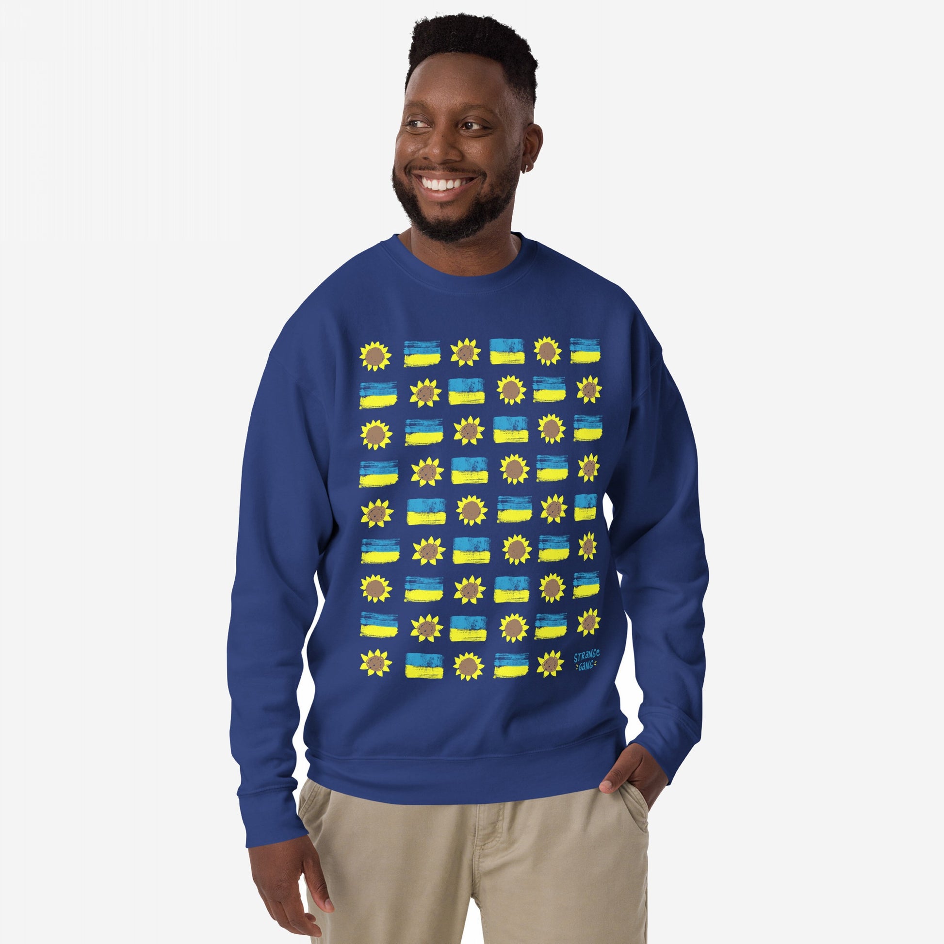Ukraine Sunflowers Sweatshirt featuring a grid of sunflower and Ukrainian flag motifs, worn by a smiling male model with light-khaki pants, embodies unity and resilience against a white backdrop.
