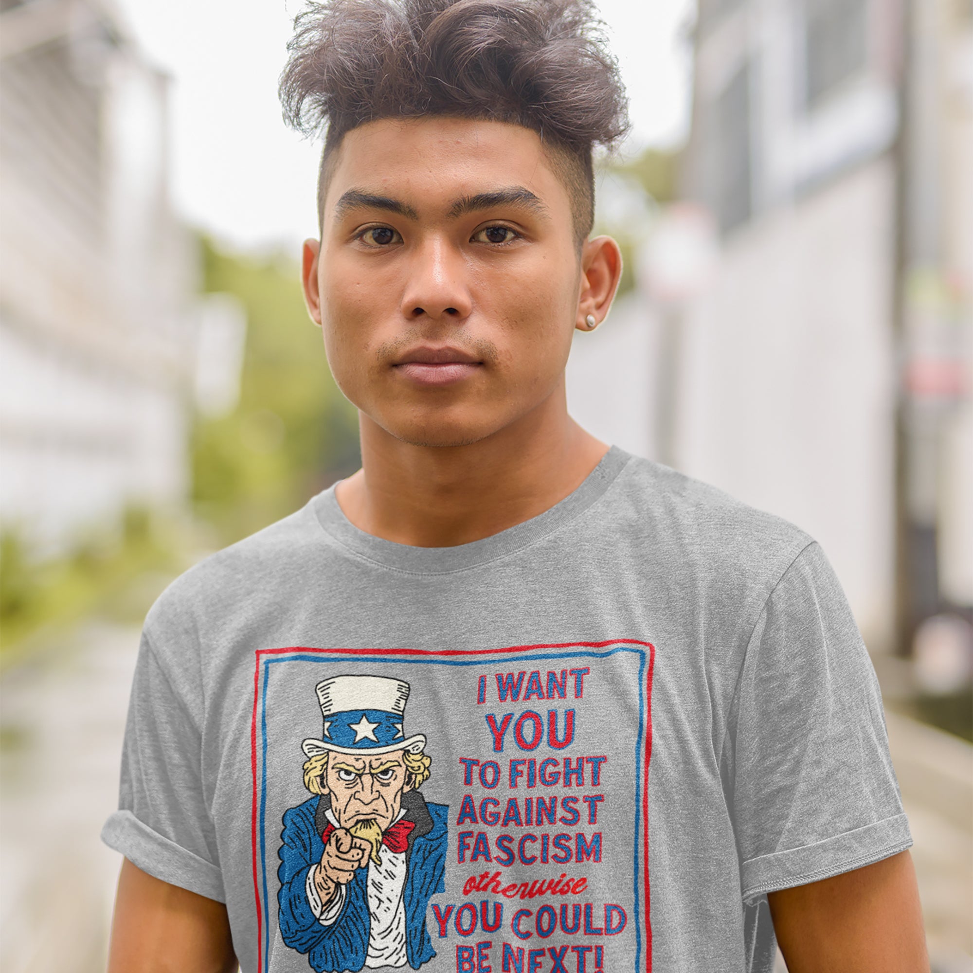 Young man wearing the Anti Fascist Uncle Sam Shirt, featuring a vintage-style Uncle Sam graphic with a bold message urging action against fascism, standing on a blurred urban street.