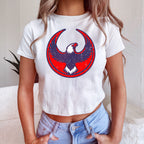 USA Rebel Alliance Women's Baby Tee features a cropped, white T-shirt with a stylized eagle emblem, paired with light-blue high-waisted jeans, embodying a bold stance on immigrant rights and equality.