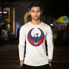 Young man wearing USA Rebel Alliance T-shirt with a stylized eagle emblem, standing on an evening street with hands in pockets, surrounded by softly lit storefronts and carts.