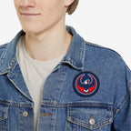 Person wearing a light-wash denim jacket displays a USA Rebel Alliance Patch on the left chest, featuring a stylized eagle, symbolizing anti-fascist and immigrant rights support, over a white T-shirt.