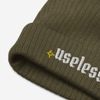 Useless Hat: Close-up of an olive-green rib knit beanie featuring “Useless” in white embroidery on the cuff, with a yellow asterisk logo. A stylish nod to embracing rest and mental well-being.