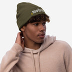 Young man wearing the Useless Hat, an olive-green knit beanie with useless embroidered in white, embodying a chill, rebellious vibe against productivity norms.