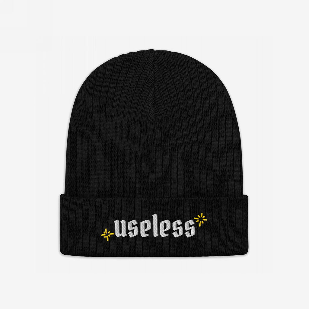 Black rib-knit beanie, labeled Useless in white Old English letters, flanked by yellow starbursts; embodies relaxation and reclaiming downtime as a revolutionary act.