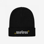 Black rib-knit beanie, labeled Useless in white Old English letters, flanked by yellow starbursts; embodies relaxation and reclaiming downtime as a revolutionary act.