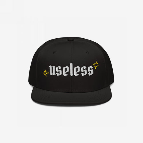 The Useless Hat features a flat-bill snapback design, with useless embroidered in white Old English font, flanked by yellow starbursts, embodying a relaxed, rebellious spirit.