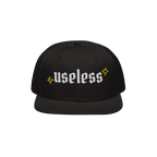 The Useless Hat features a flat-bill snapback design, with useless embroidered in white Old English font, flanked by yellow s