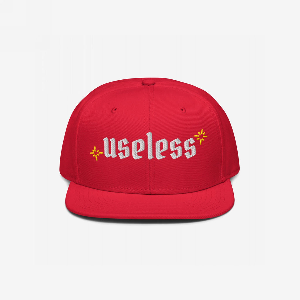 Useless Hat: A red snapback cap with useless in white Old English font, flanked by yellow starbursts, promoting relaxation and self-care with a bold, unapologetic statement.
