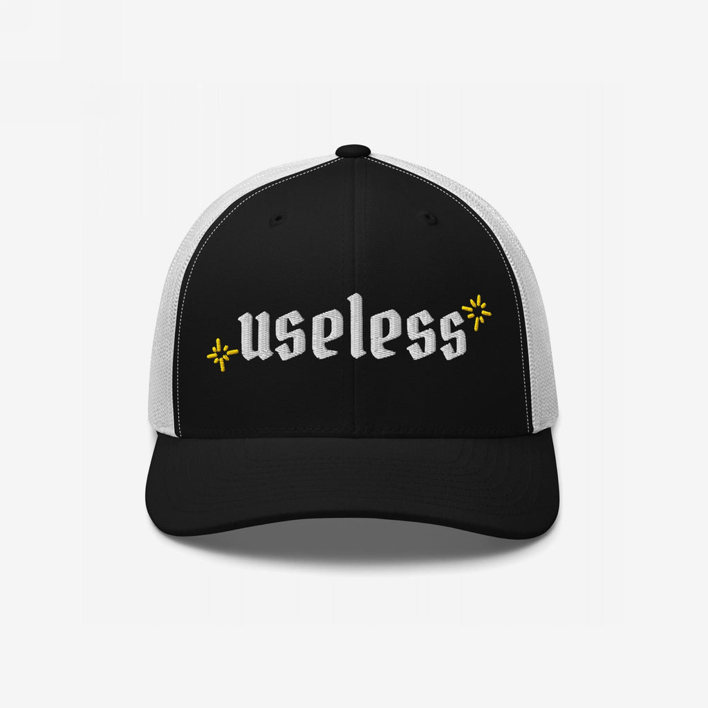 The Useless Hat, a two-tone trucker cap, features useless in bold Old English font on black fabric, flanked by yellow starbursts, embodying a chill, revolutionary vibe.
