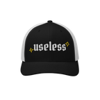 The Useless Hat, a two-tone trucker cap, features useless in bold Old English font on black fabric, flanked by yellow starbur