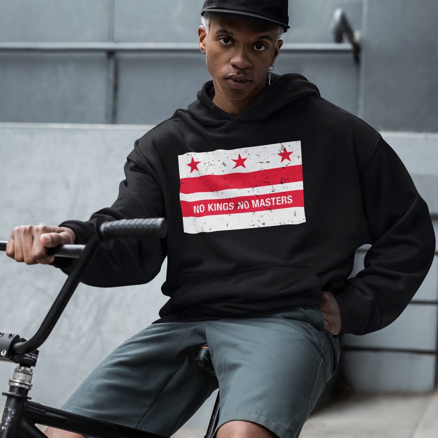 Young person on BMX bike wearing Washington DC No Kings Flag Shirt, featuring anti-authoritarian design with stars and “NO KINGS NO MASTERS” slogan, embodying bold resistance and equality.
