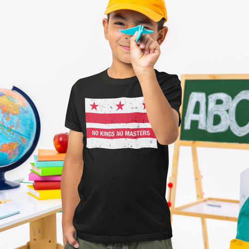 Boy in classroom holds a blue paper airplane while wearing Washington DC No Kings Flag Shirt, featuring red stars and stripes