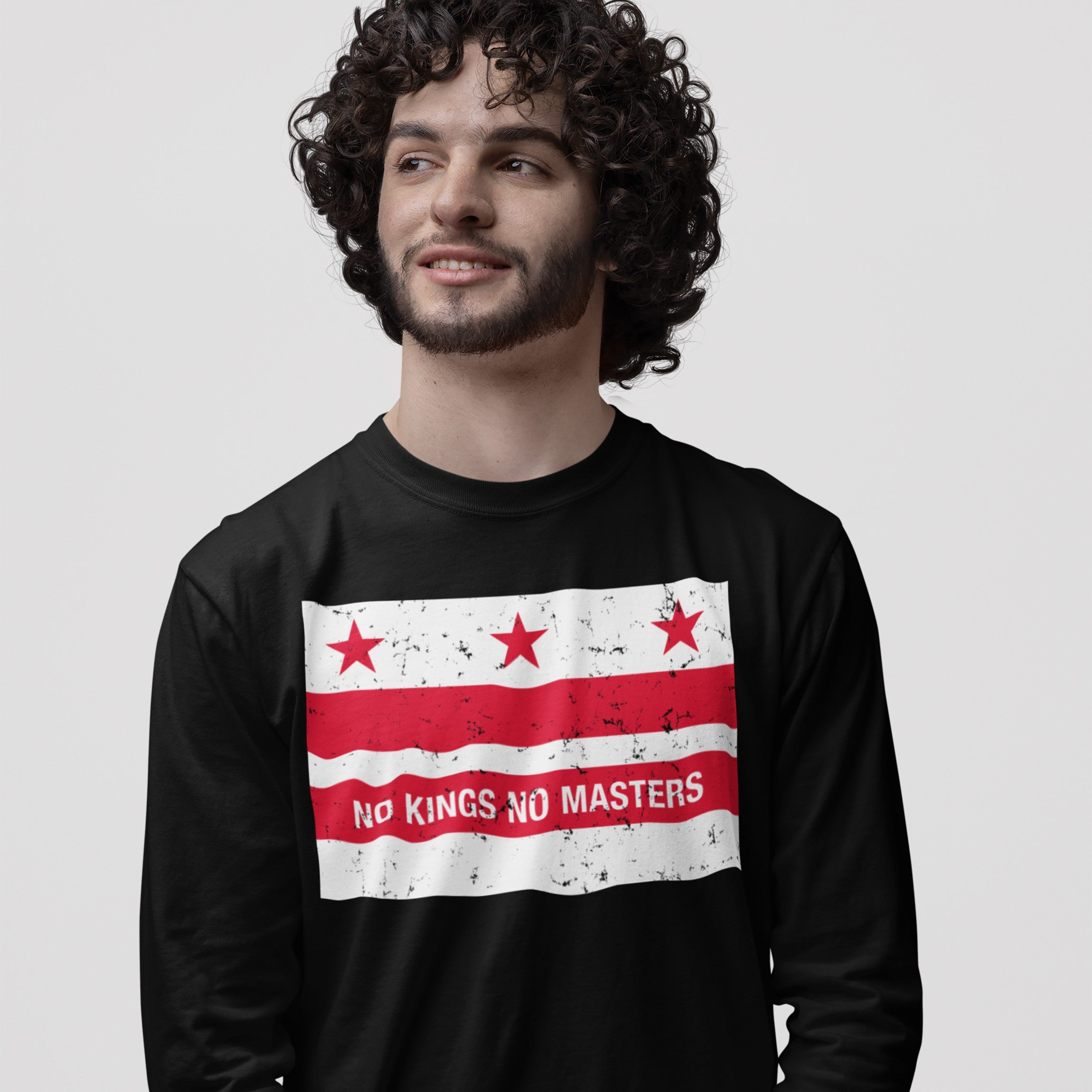 Young man wearing the Washington DC No Kings Flag Shirt featuring a distressed red and white flag graphic with No Kings No Masters slogan, embodying a bold anti-authoritarian message against a light background.