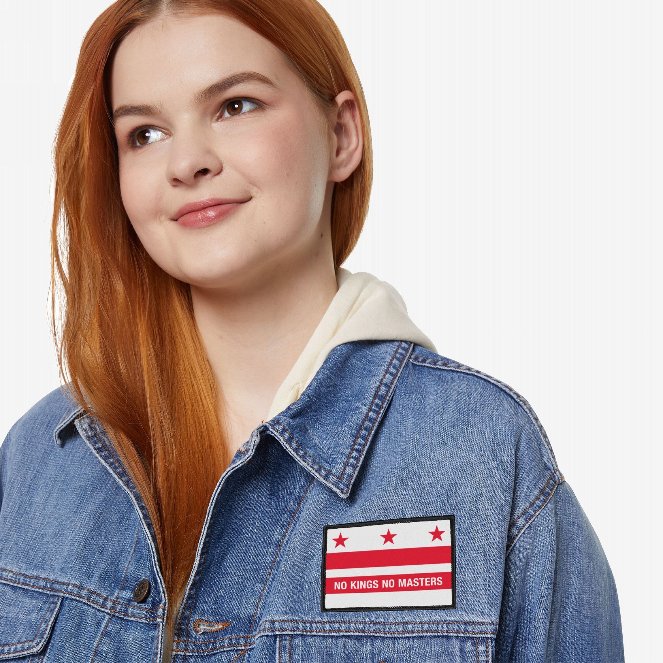 Young woman wears cream hoodie and blue denim jacket with a Washington DC Flag No Kings Patch, featuring red stars and stripes. The patch embodies anti-hierarchical sentiment, supporting grassroots resistance.