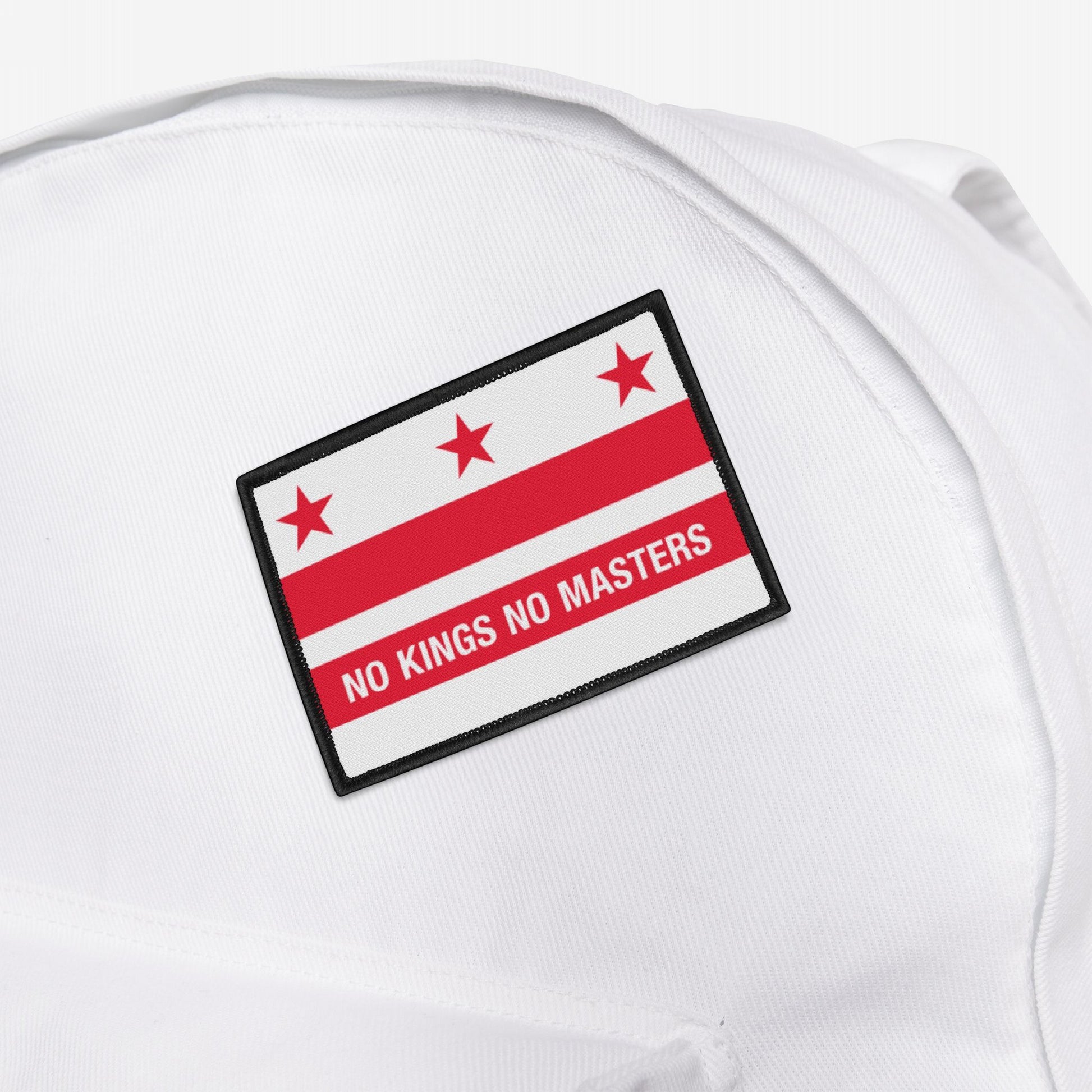 White fabric backpack featuring the Washington DC Flag No Kings Patch, embroidered with “NO KINGS NO MASTERS.” The patch advocates for equality and justice, aligning with grassroots resistance values.