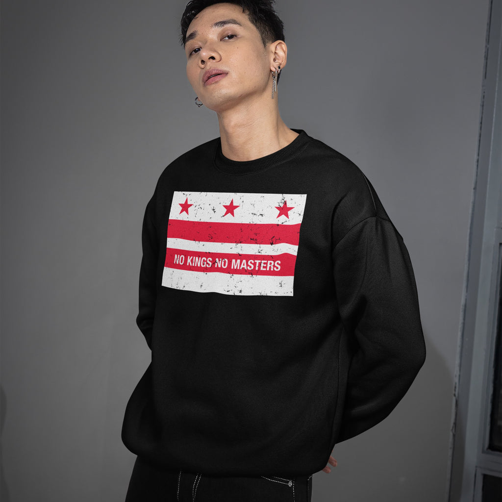 Young man in black Washington DC No Kings Flag Shirt with red stars and stripes, slogan NO KINGS NO MASTERS, embodying anti-authoritarian spirit; hands behind back, small hoop earrings.