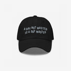 Wasted Days Hat featuring bold embroidery with the phrase “A DAY NOT WASTED IS A DAY WASTED” on a black cap, embodying a carefree, rebellious spirit perfect for endless adventures.