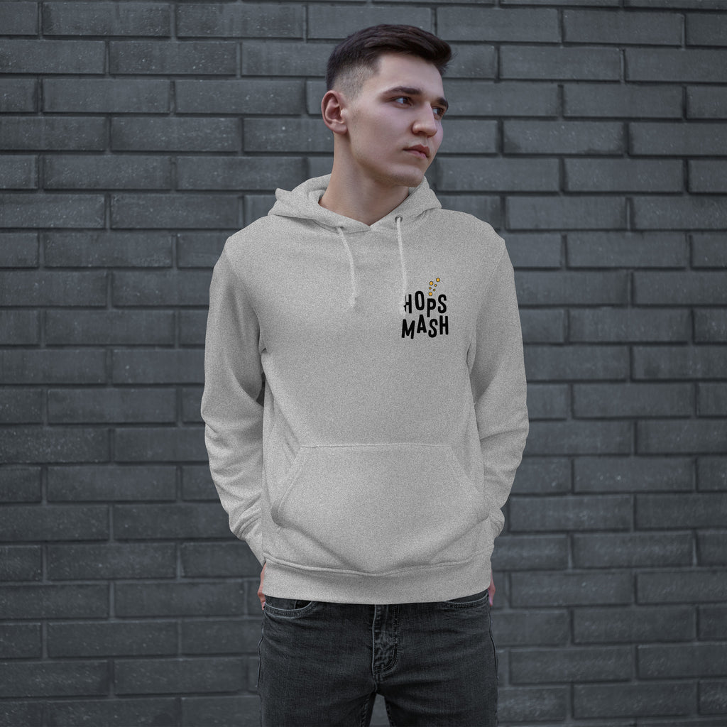 Young man wearing the Wasted Days Hoodie, featuring a subtle “HOPS MASH” logo on the chest, embodies an urban vibe against a brick wall, hands in the kangaroo pocket, looking contemplative.