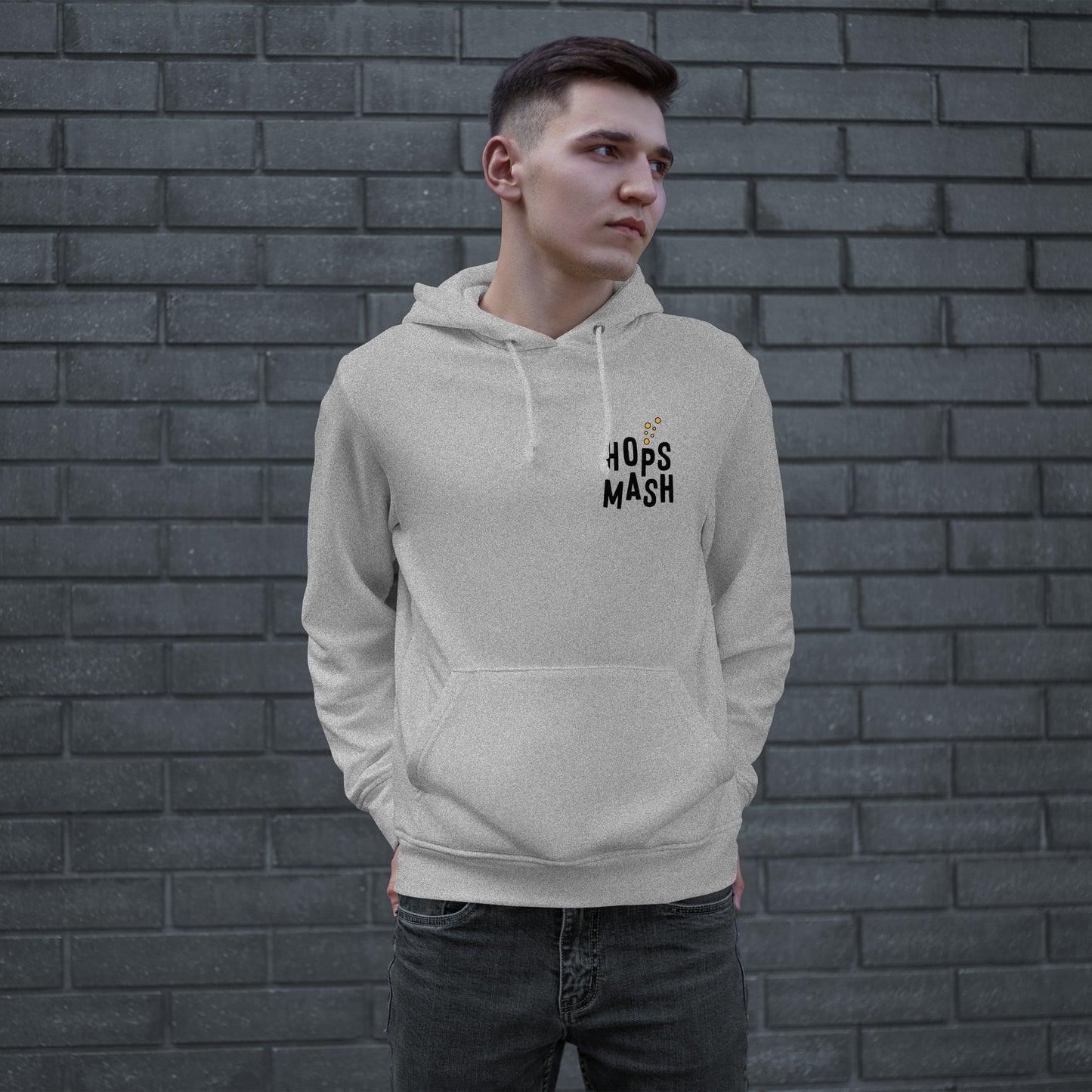 Young man wearing the Wasted Days Hoodie, featuring a subtle “HOPS MASH” logo on the chest, embodies an urban vibe against a brick wall, hands in the kangaroo pocket, looking contemplative.