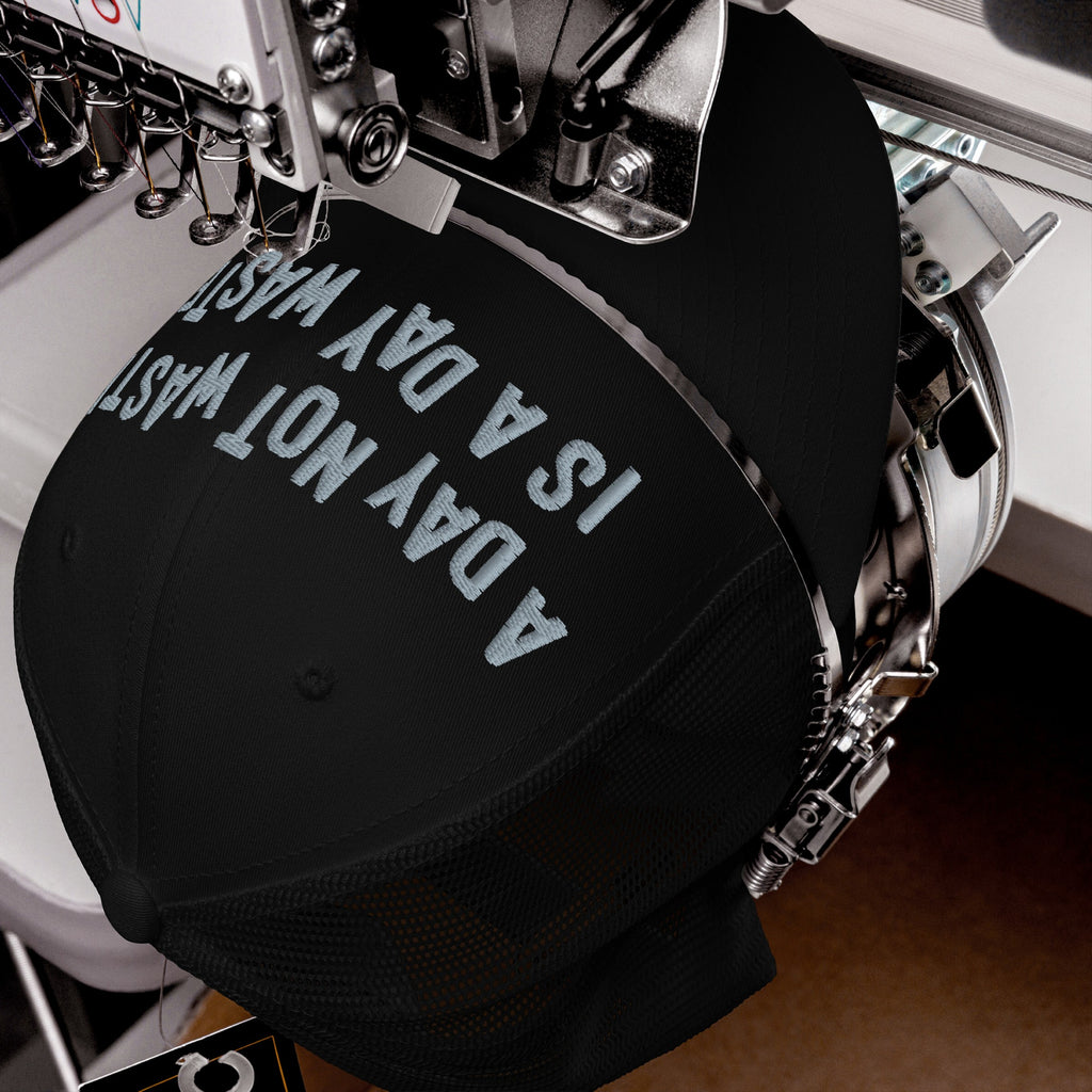 Wasted Days Hat being embroidered with “A DAY NOT WASTED” on a black cap by a machine, capturing the carefree and bold essence of living unapologetically.