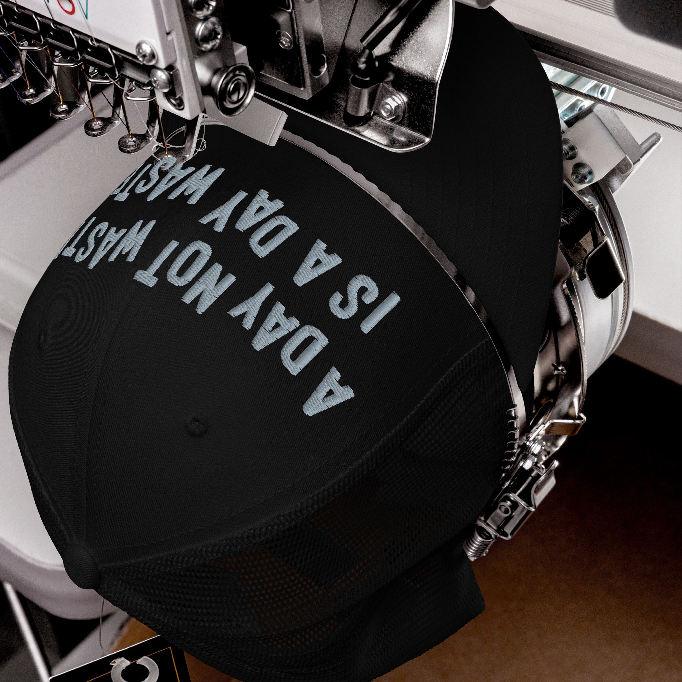 Wasted Days Hat being embroidered with “A DAY NOT WASTED” on a black cap by a machine, capturing the carefree and bold essence of living unapologetically.