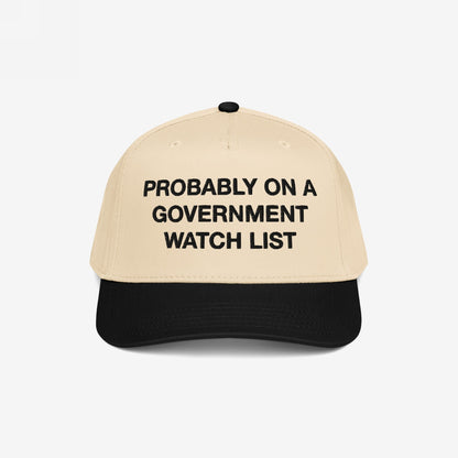 The Watch List Hat features a beige crown with a black brim. Bold black letters declare, PROBABLY ON A GOVERNMENT WATCH LIST, embodying a bold statement on visibility and resistance.