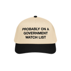 The Watch List Hat features a beige crown with a black brim. Bold black letters declare, PROBABLY ON A GOVERNMENT WATCH LIST,