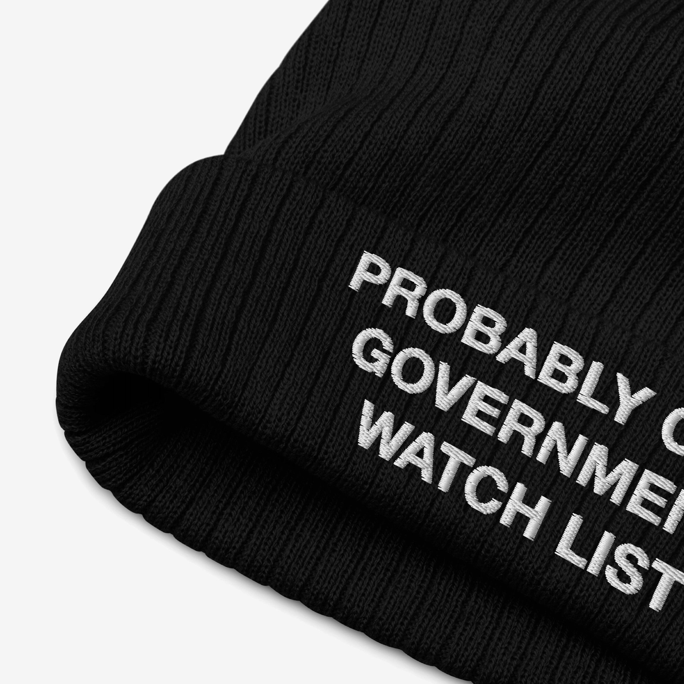 The Watch List Hat is a black rib-knit beanie featuring bold white embroidery, PROBABLY ON GOVERNMENT WATCH LIST, emphasizing protest and advocacy. Ideal for those engaging in social justice actions.