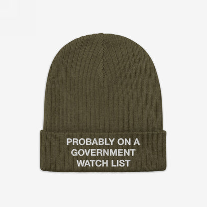 The Watch List Hat features an olive-green, ribbed knit design with a folded cuff, embroidered with “PROBABLY ON A GOVERNMENT WATCH LIST,” reflecting bold activism and individuality.