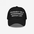 The Watch List Hat features a black baseball style with white embroidered text stating, PROBABLY ON A GOVERNMENT WATCH LIST, highlighting bold protest and individuality with its unstructured crown and curved brim.