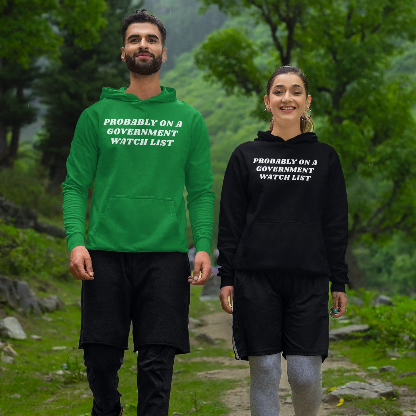 Two young adults wear Watch List Hoodie & Sweatshirt with bold text, PROBABLY ON A GOVERNMENT WATCH LIST, while walking on a forest trail, embodying defiance and advocacy for equality.