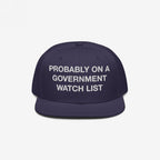 Watch List Hat: A dark navy snapback cap with white block letters, stating PROBABLY ON A GOVERNMENT WATCH LIST, embodying bold protest spirit and advocacy for visibility and accountability.